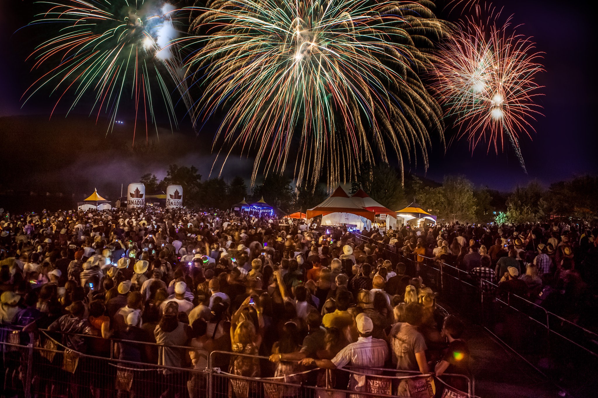 a giant outdoor crowd looks up at the huge blasts of the colourful fireworks display in the night sky above their heads at Mattawa Voyageur Days.