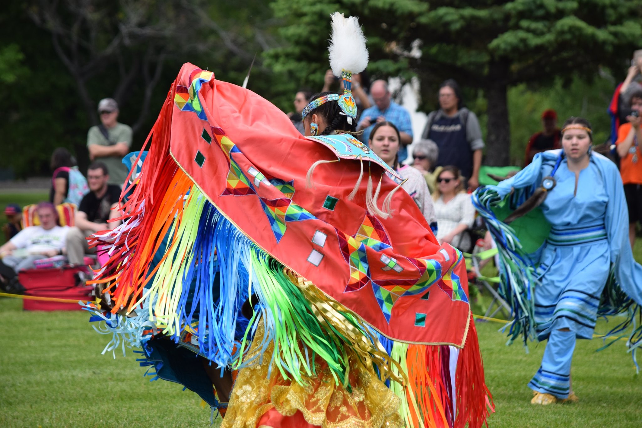 A woman in beautiful, colourful regalia dances with her shawl spread wide at the N'Swakamok National Indigenous Peoples Day Pow Wow