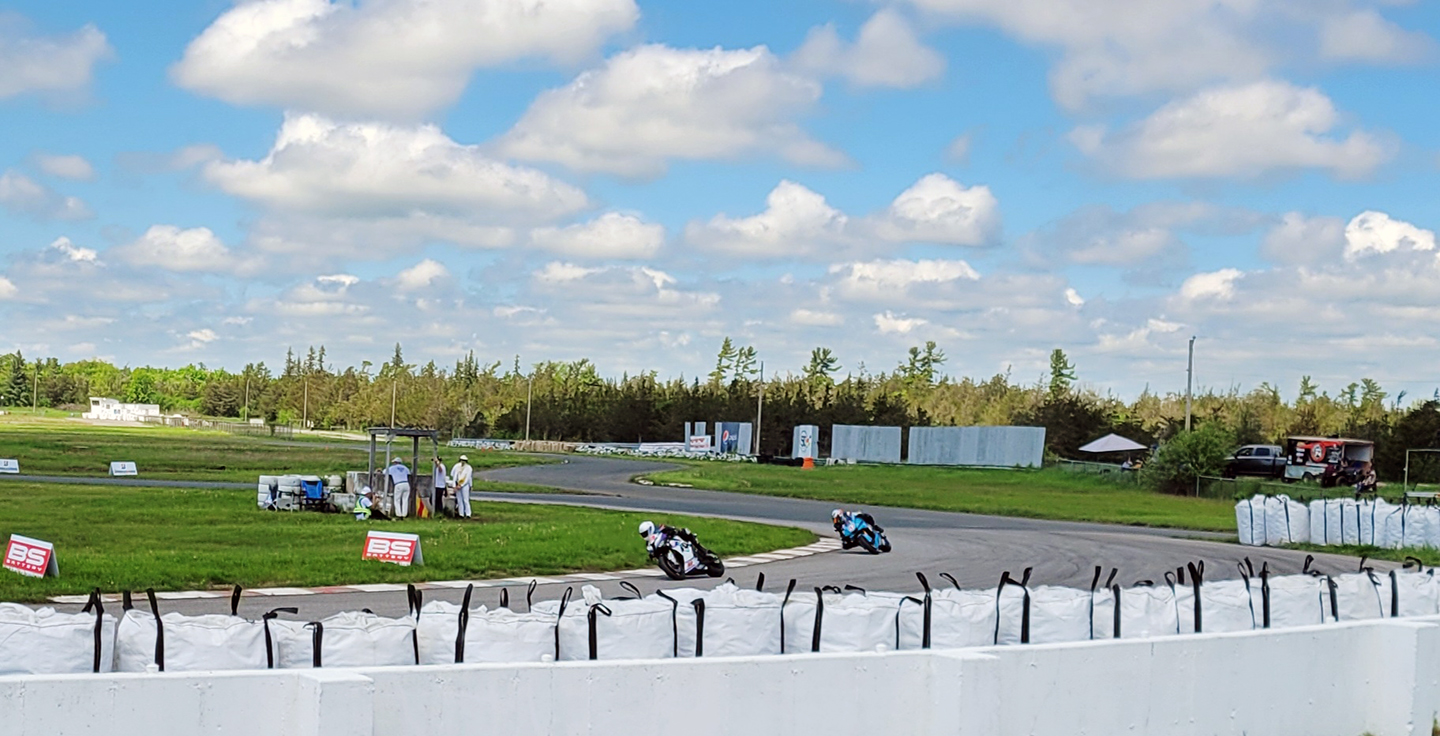 2 superbikes racing around a bend in the track at a racing event on a rummer day.