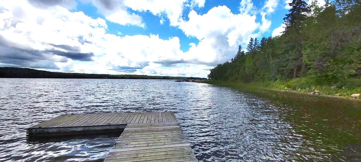 a wooden dock at Restoule Provincial Park, which extends out into a calm lake that is surrounded by green forest.