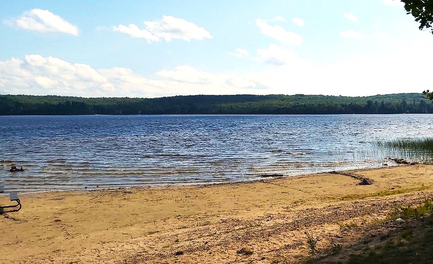 a long, sandy beach along a blue lake surrounded by green forest on a sunny summer day at Restoule Provincial Park.