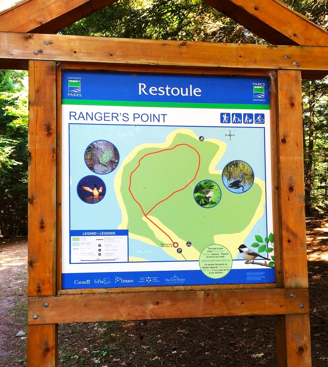 A sign framed by wooden beams that reads "Restoule, Ranger's Point" and has a coloured map of the Ranger's Point hiking trail. Forest is in the background.