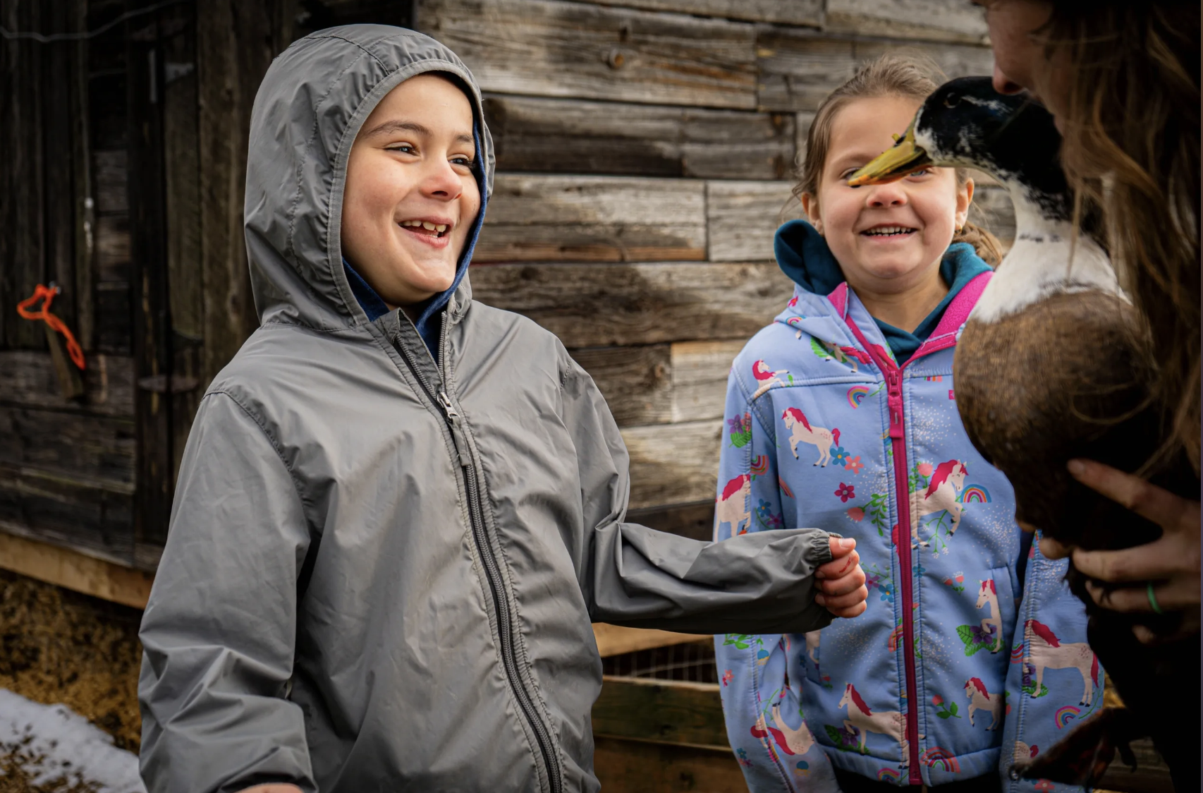 Two children smiling and looking at a duck.