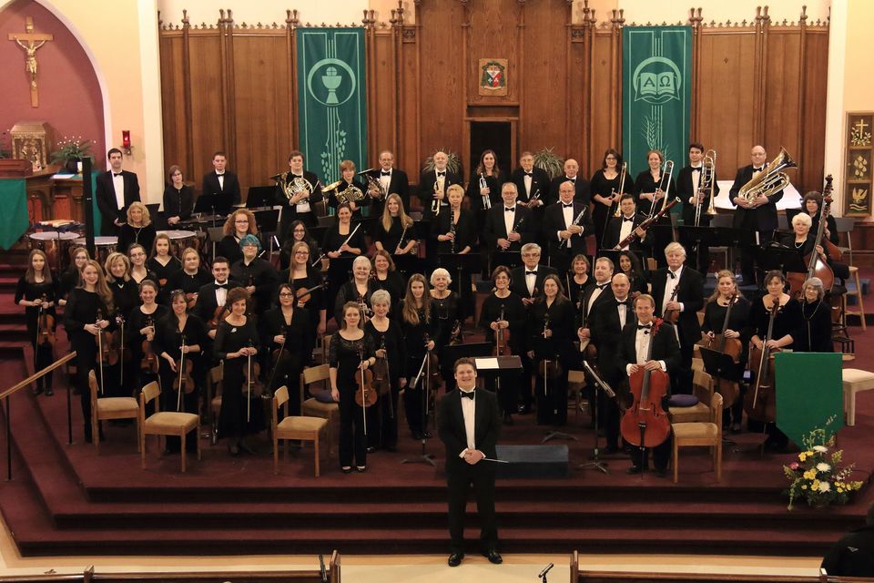 A wide view of all the members from the Timmins symphony orchestra holding their instruments and smiling at the camera