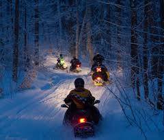 peoples who are snowmobiling one behind the other down a tree-lines trail of snow