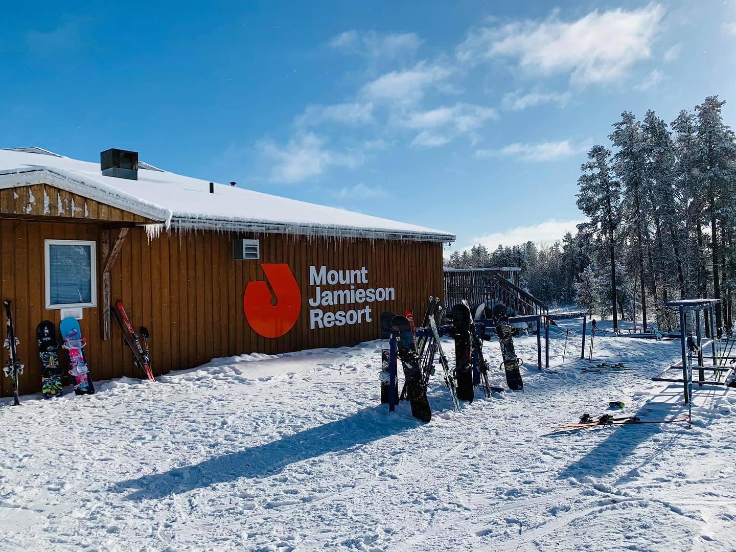 a wide view of the side of the Mount Jamieson Resort lodge with snow on the ground and snowboards sticking out of it in front of the side of the building