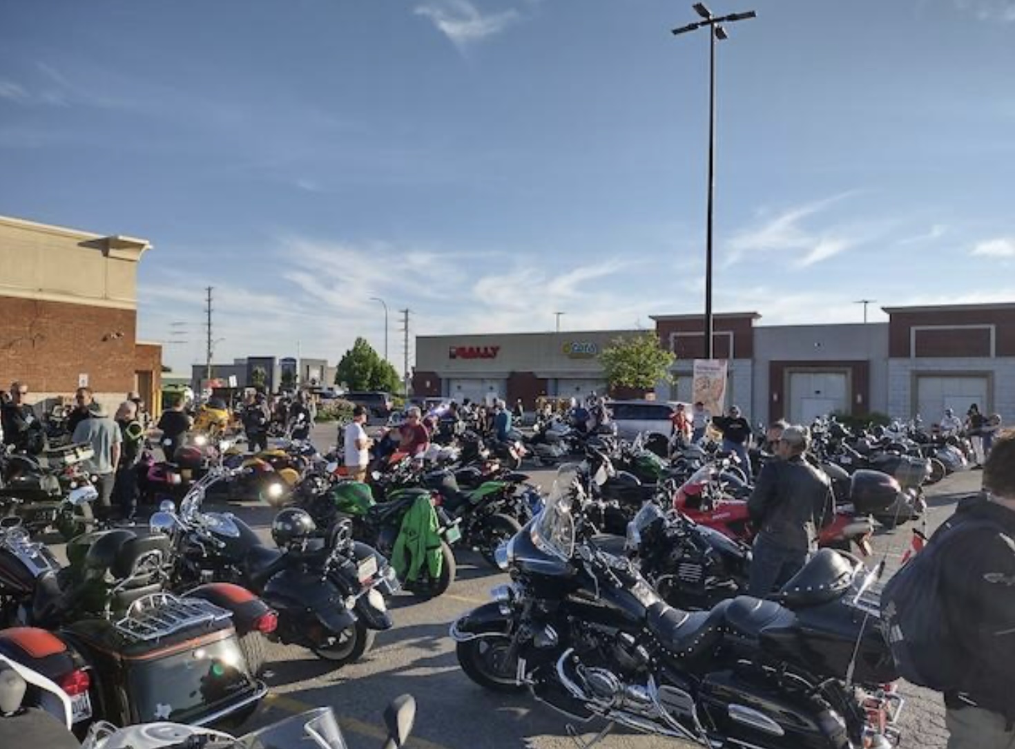 A strip mall parking lot on a summer afternoon filled with rows of parked motorcycles.