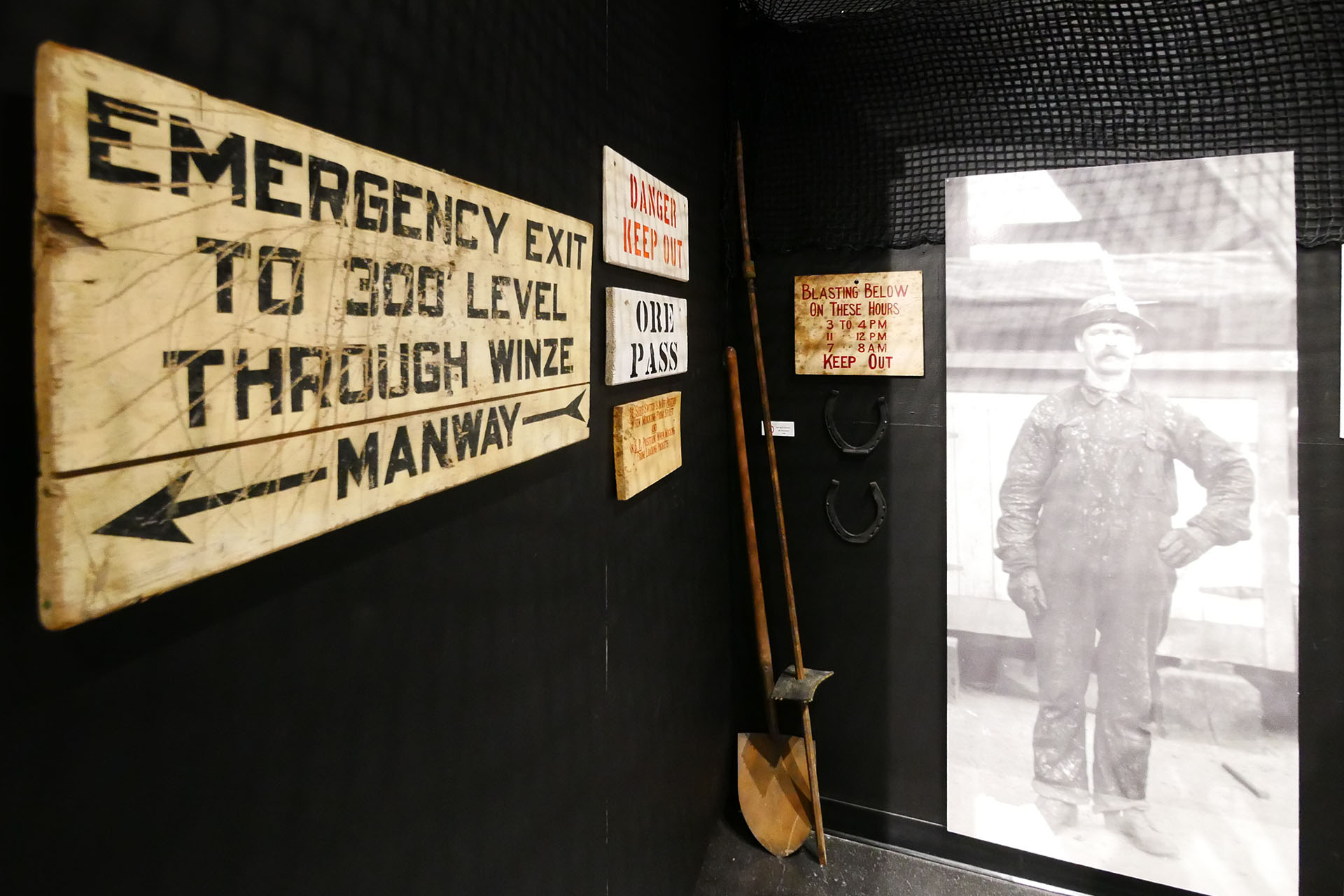 Old wooden mining signs and a large black and white photograph of a man in a wool uniform and miner's helmet, part of a mining exhibit.