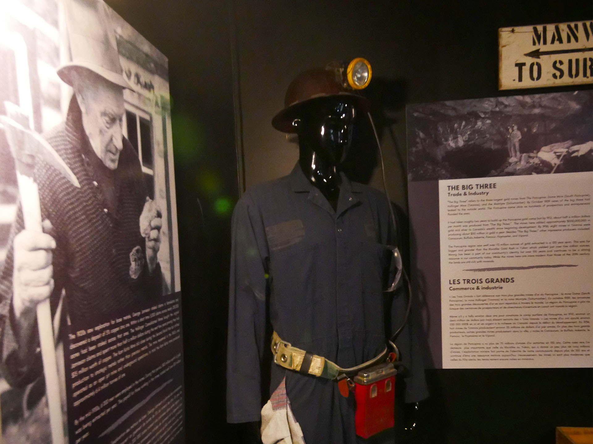 A black and white interpretive poster and antique mining uniform on a mannequin, part of the exhibits at the mining museum in Timmins. 