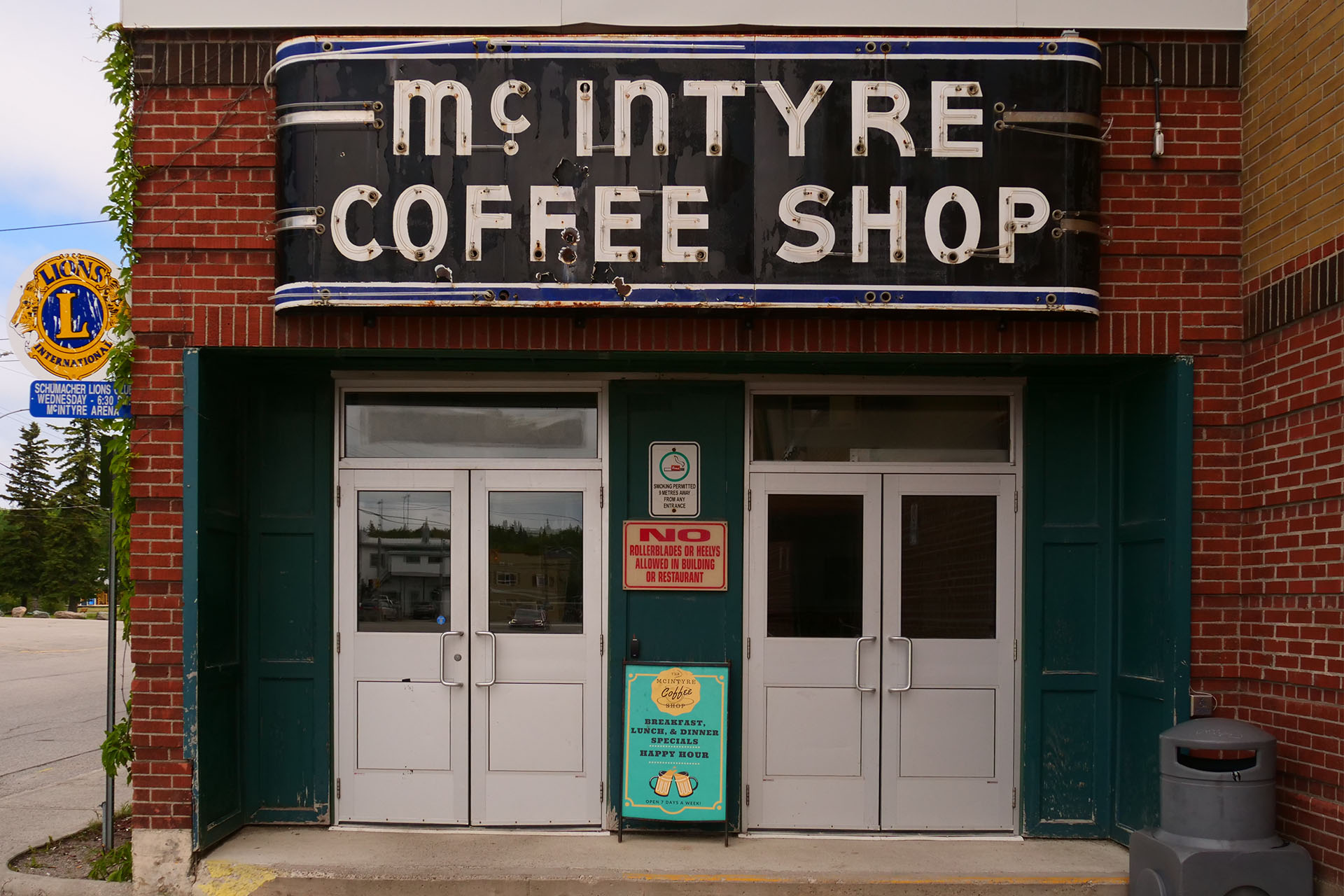 A little building with two sets of double doors, painted white with green borders, and a sign above in a style reminiscent of the 1930s that reads "McIntyre Coffee Shop".