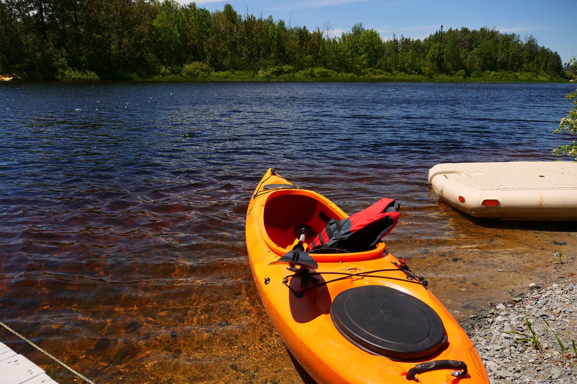 A yellow kayak and a paddleboard at the edge of the Mattagami River on a summer day.. 