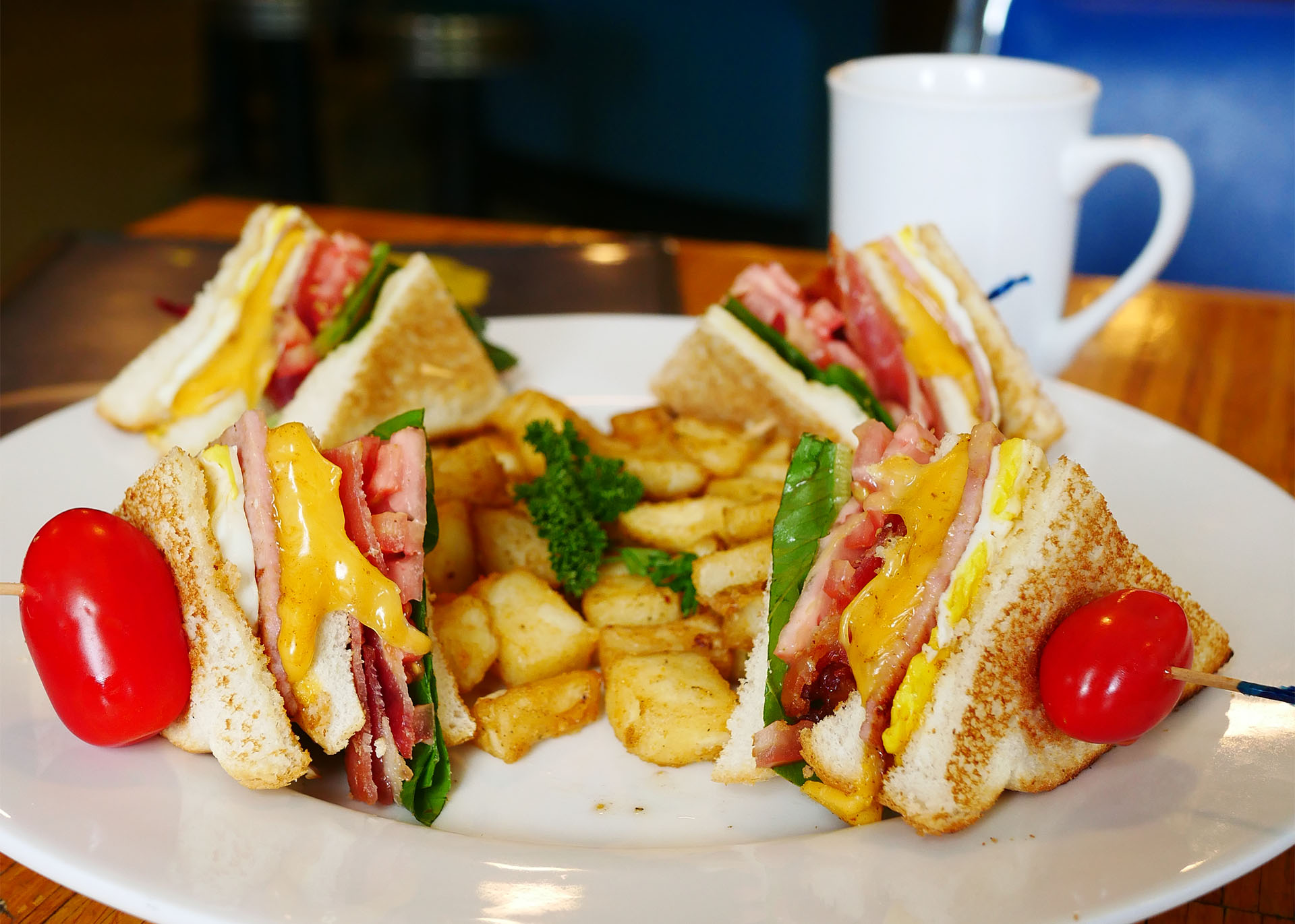 a delicious club sandwich with fries on a white plate with a cup of coffee to the side. 