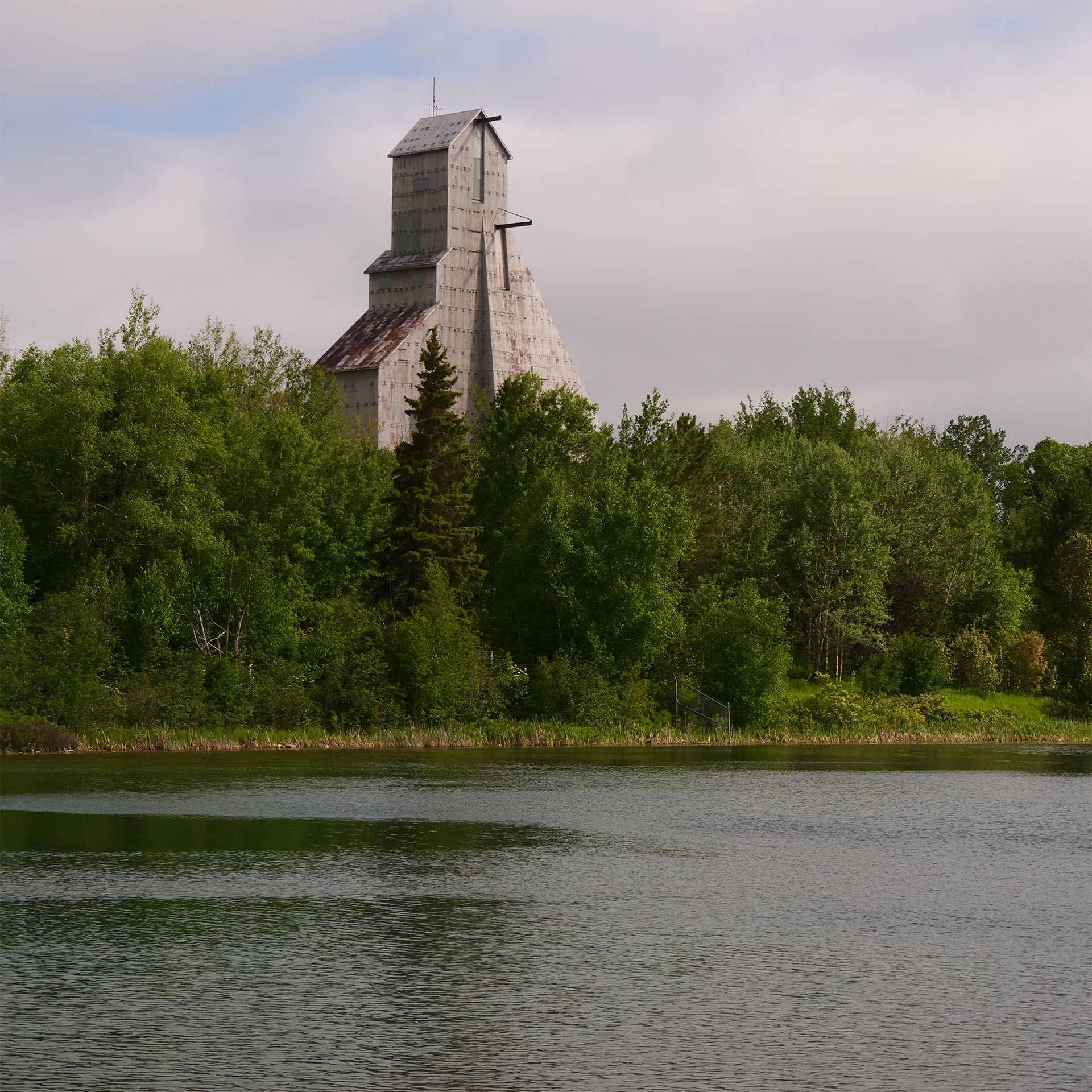 The McIntyre Headframe standing tall above a green forest on the other side of a calm lake.