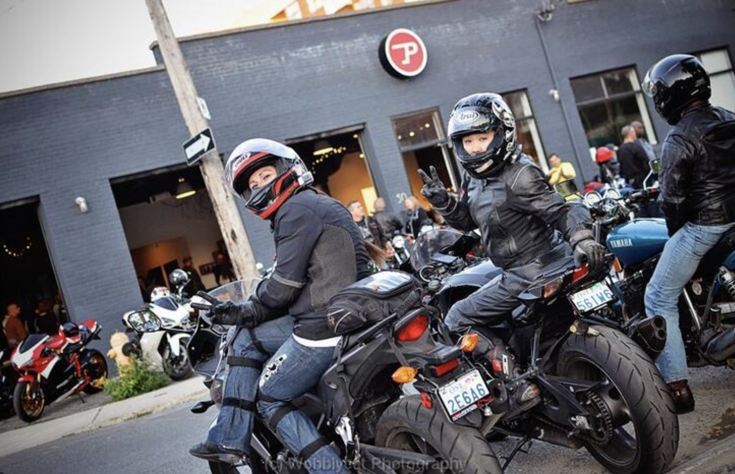 3 motorcyclists parked in front of a restaurant. Two are turned around in their seats to look at the camera.