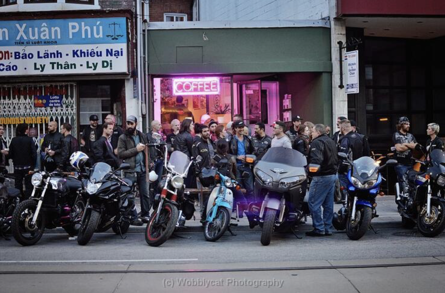a long row of motorcycles parked side by side in front of a restaurant, with a large crowd of bikers chatting on the sidewalk.