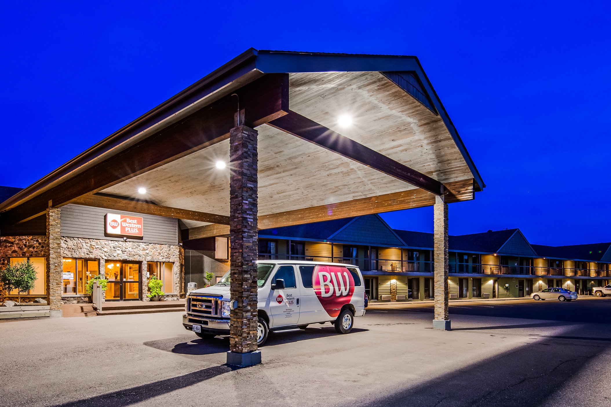 The front entrance to a one story hotel at night. There is a white van in the foreground. 