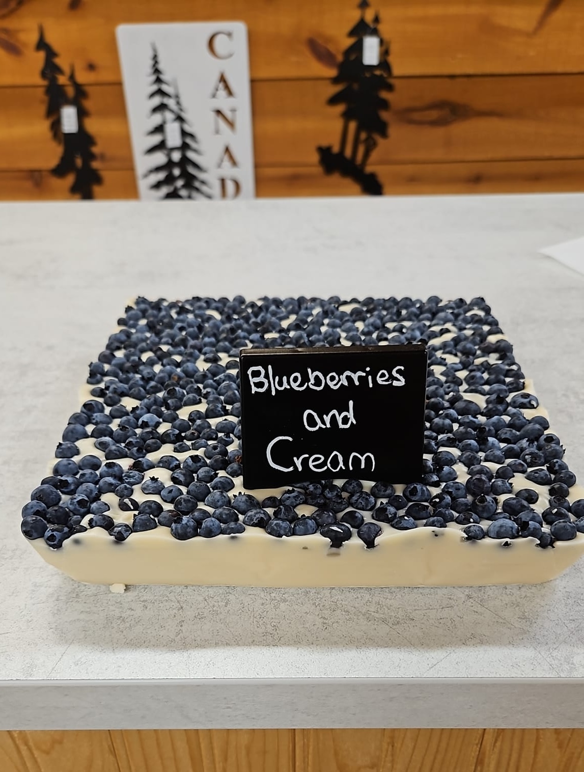 white handmade fudge, full of whole blueberries, sitting in a large block on a counter at French River Trading Post. It sports a label that reads "Blueberries and Cream".