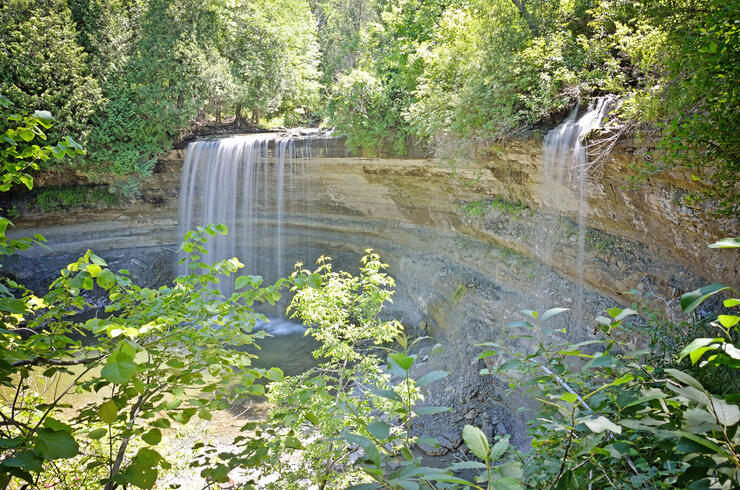 Bridal Veil Falls; a gentle, misty falls that creates a veil of water that decends off a cliff into a rocky pool below. The falls is surrounded by lush green foliage. 