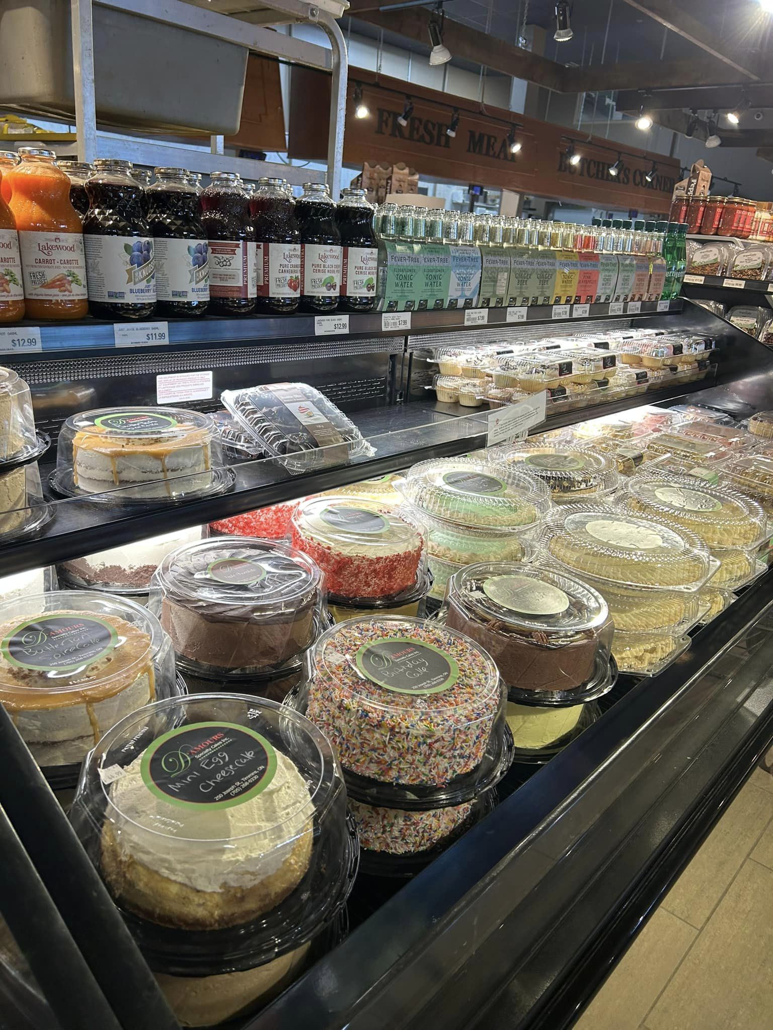 Close-up of the various cakes on display at the Pick of The Crop Grocery Store with canned items on top that are also on display