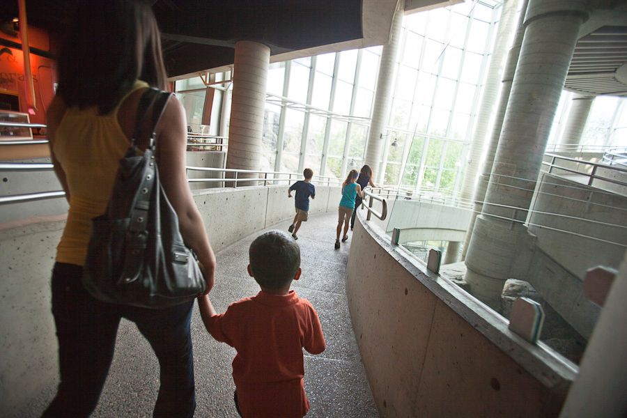 A mother and children run along a pedway in a large sunny exhibit room at Science North.