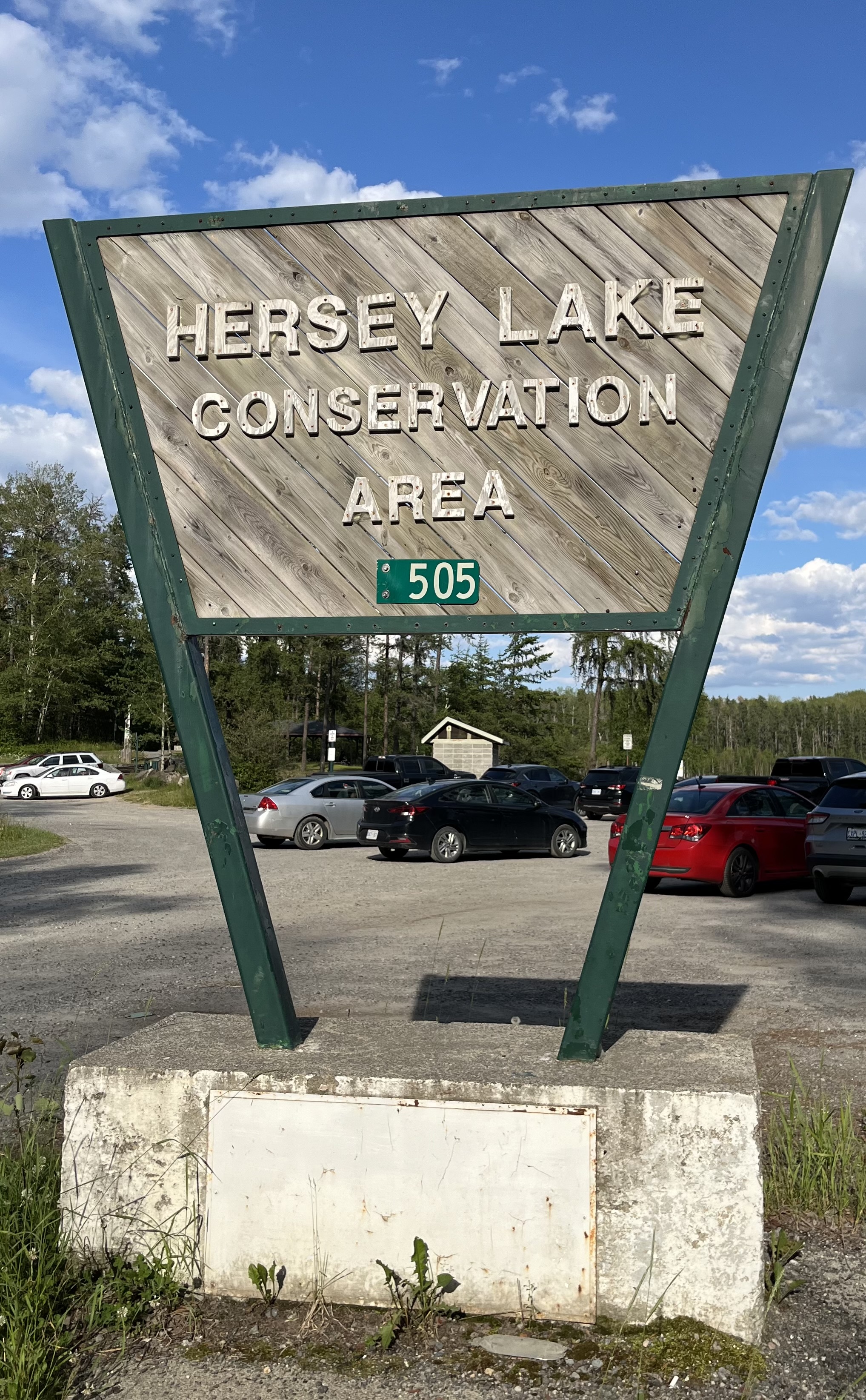 a close-up of the Hersey Lake Conservation Area sign which is displayed at the entrance of the parking lot at Hersey Lake. It includes the letters 505 for its address and there is a red, black, silver and white car in the background