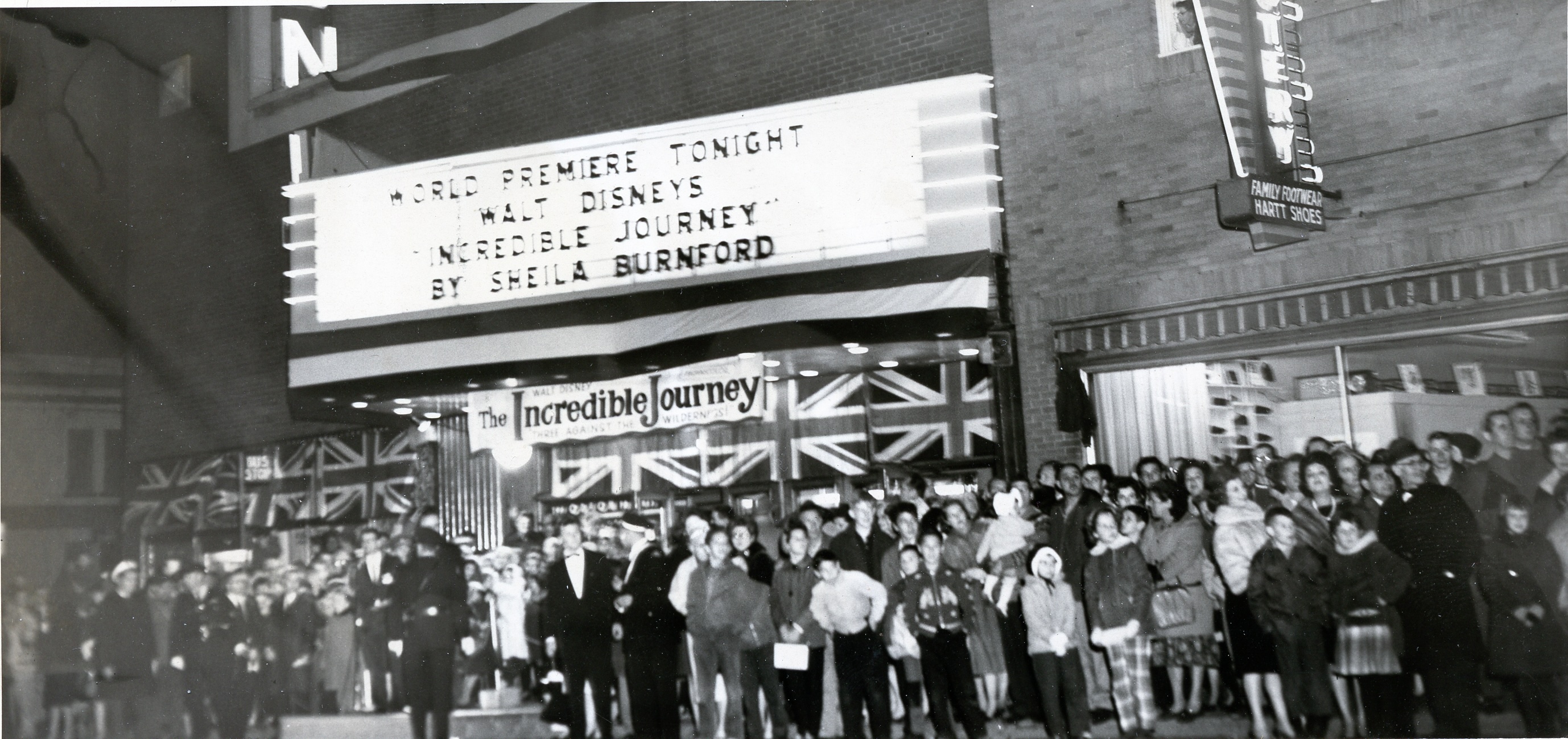 A black and white photo of a huge crowd lined up outside the theatre at Port Arthur to see the 1963 premiere of The Incredible Journey. The lit box office sign above the crowd reads "world premiere tonight: Walt Disneys 'Incredible Journey' by Sheila Burnford". 