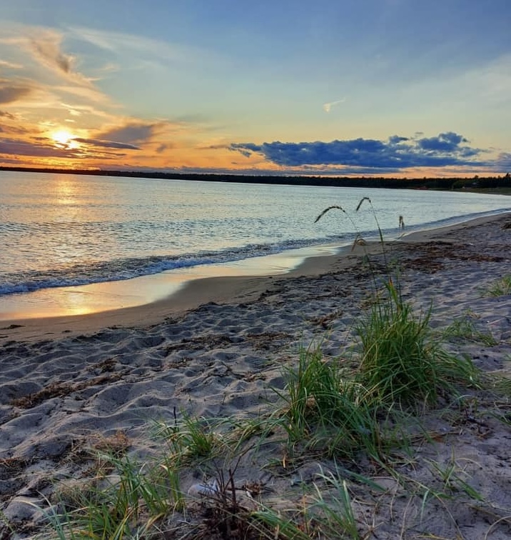 Providence Bay Beach at sunset; a white sand beach with calm glassy water under an orange sunset.