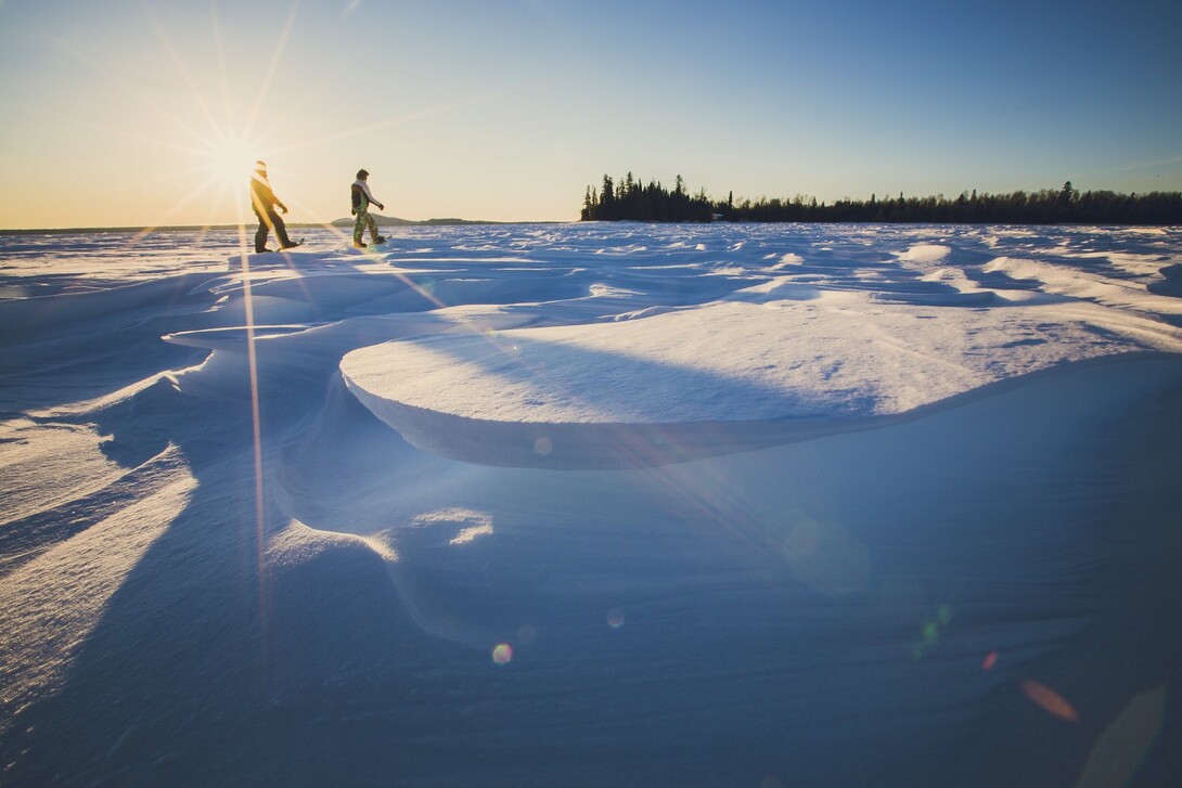 Two snowshoers moving across a frozen lake at sunset.