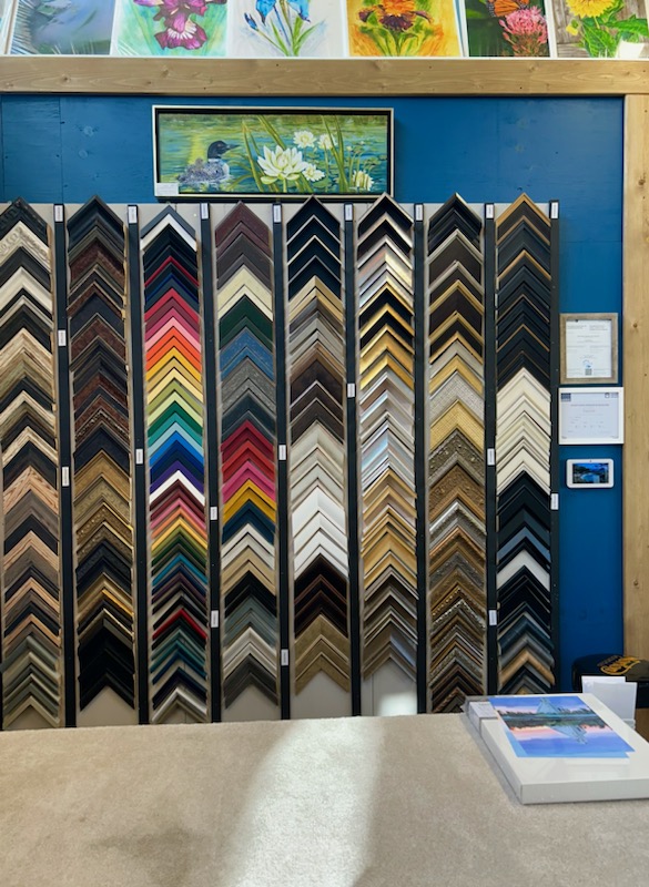 triangles are placed one on top of each other onto a rectangular panel which is placed side by side to make a total of eight panels. All of the triangles vary in colour and this is hung on the wall behind the counter and below various frames pictures