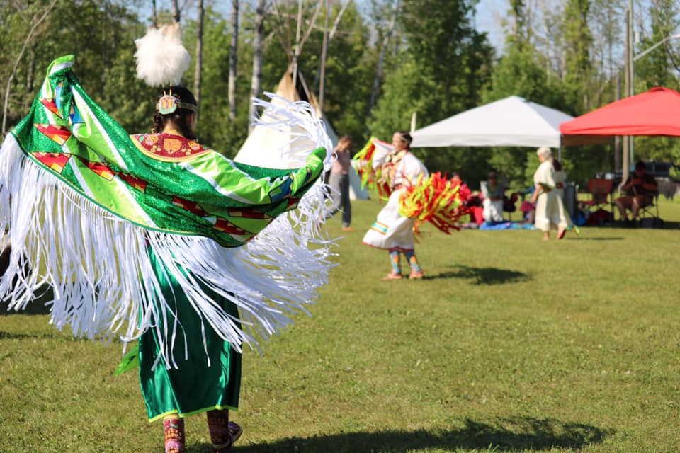 two girls in beautifully coloured, beaded regalia dance in the grassy pow wow grounds at the Sheguiandah Annual Jiingtamok.