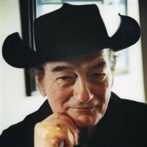 Stompin' Tom Connors in a black shirt and cowboy hat, looking thoughtful.