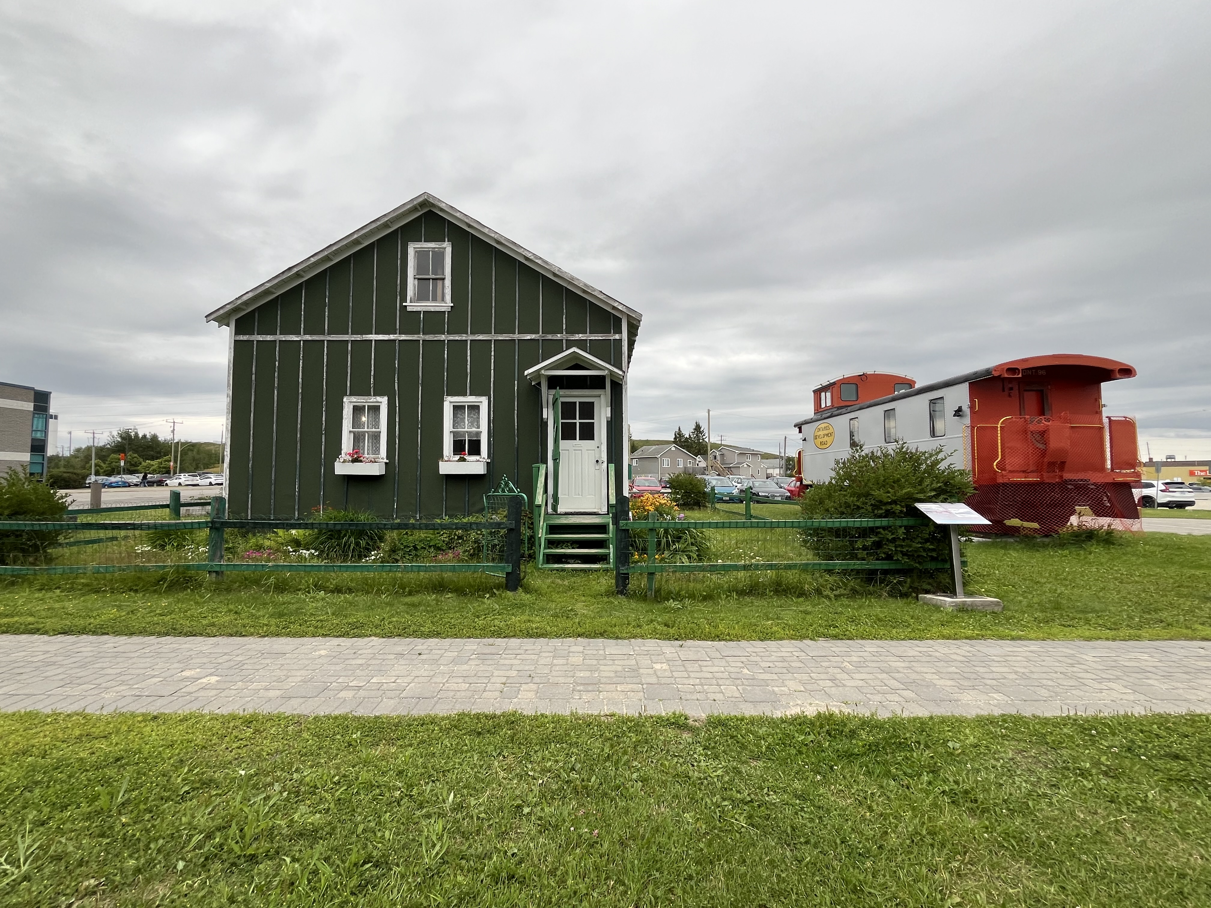 on the left-hand side is the green Hollinger House and on the right-hand side is the orange train which is situated behind the sidewalk that leads to the museum