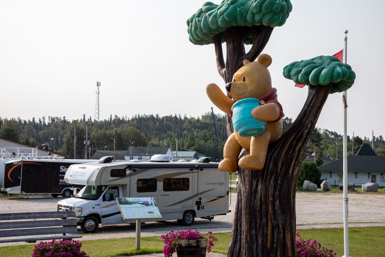 A coloured statue of Winnie the Pooh sitting in a tree with a honey pot found in White River, with an RV parked below it. 