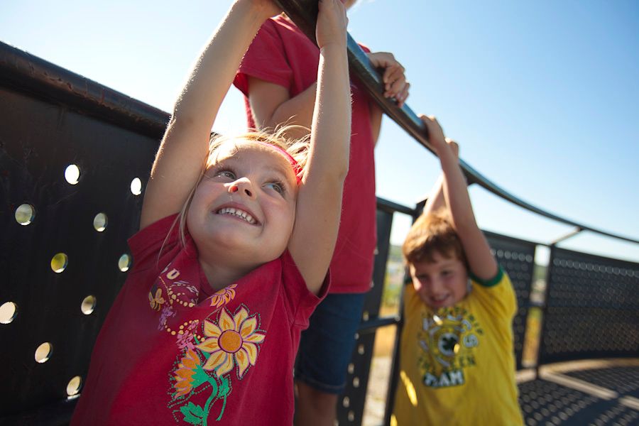 Kids smiling and swinging on playground equipment on a sunny summer day.