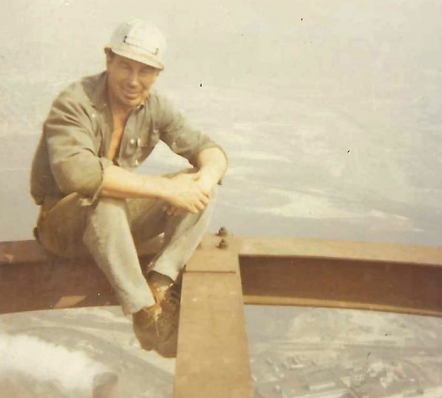 A construction worker with no safety gear atop a steel girder.