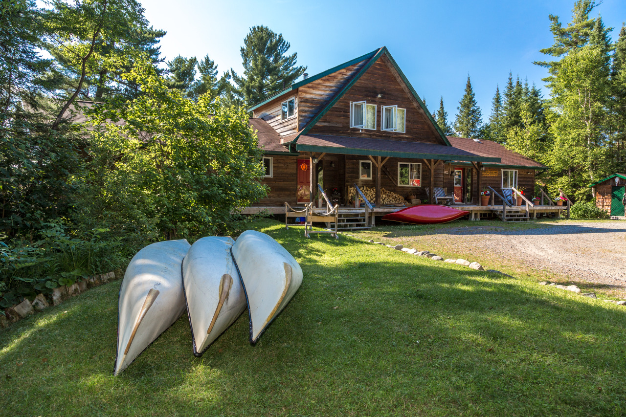 3 metal canoes lined up on the green grass next to a wooden cabin at Smoothwater Outfitters. 