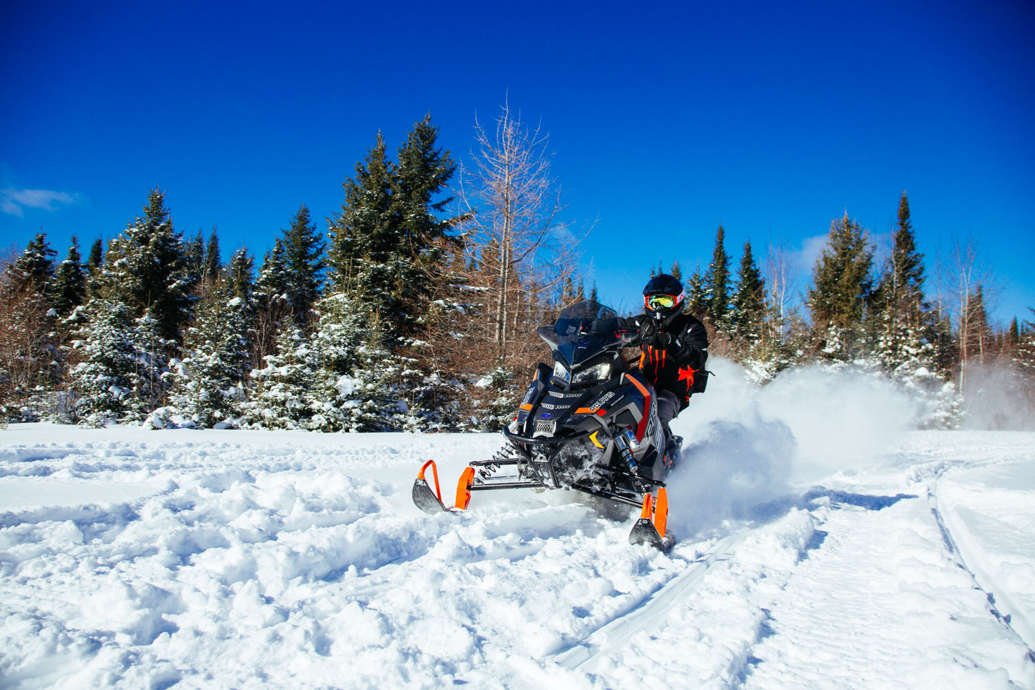 a close-up of someone snowmobiling down a snowmobile trail with a black and orange snowmobile and is also wearing a black and orange coat