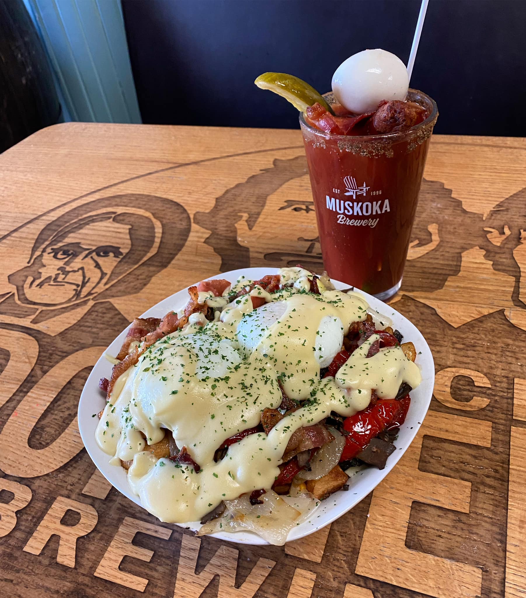 Eggs benedict on a plate next to a Caesar on a wooden table.