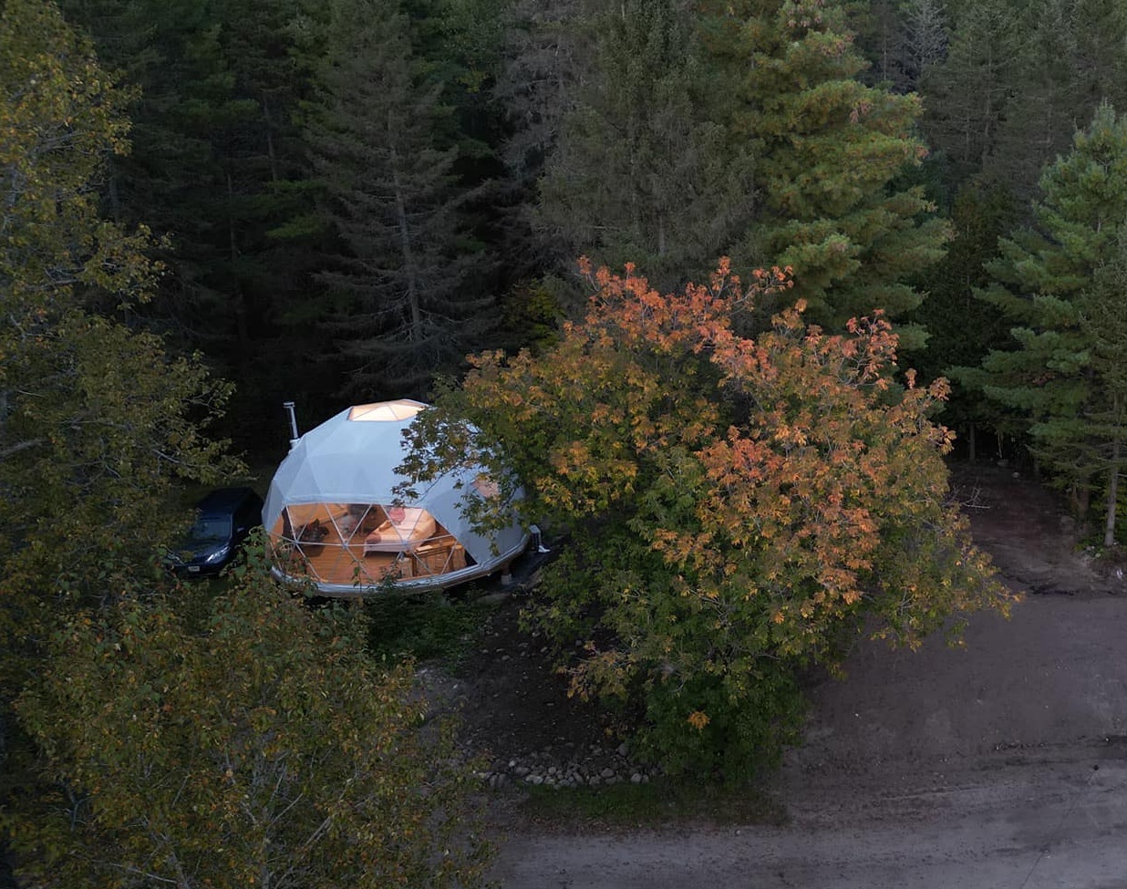 an aerial shot of an illumintaed glamping dome at Otter Pointe Resort, the tops of the leaves beginning to turn red and yellow.