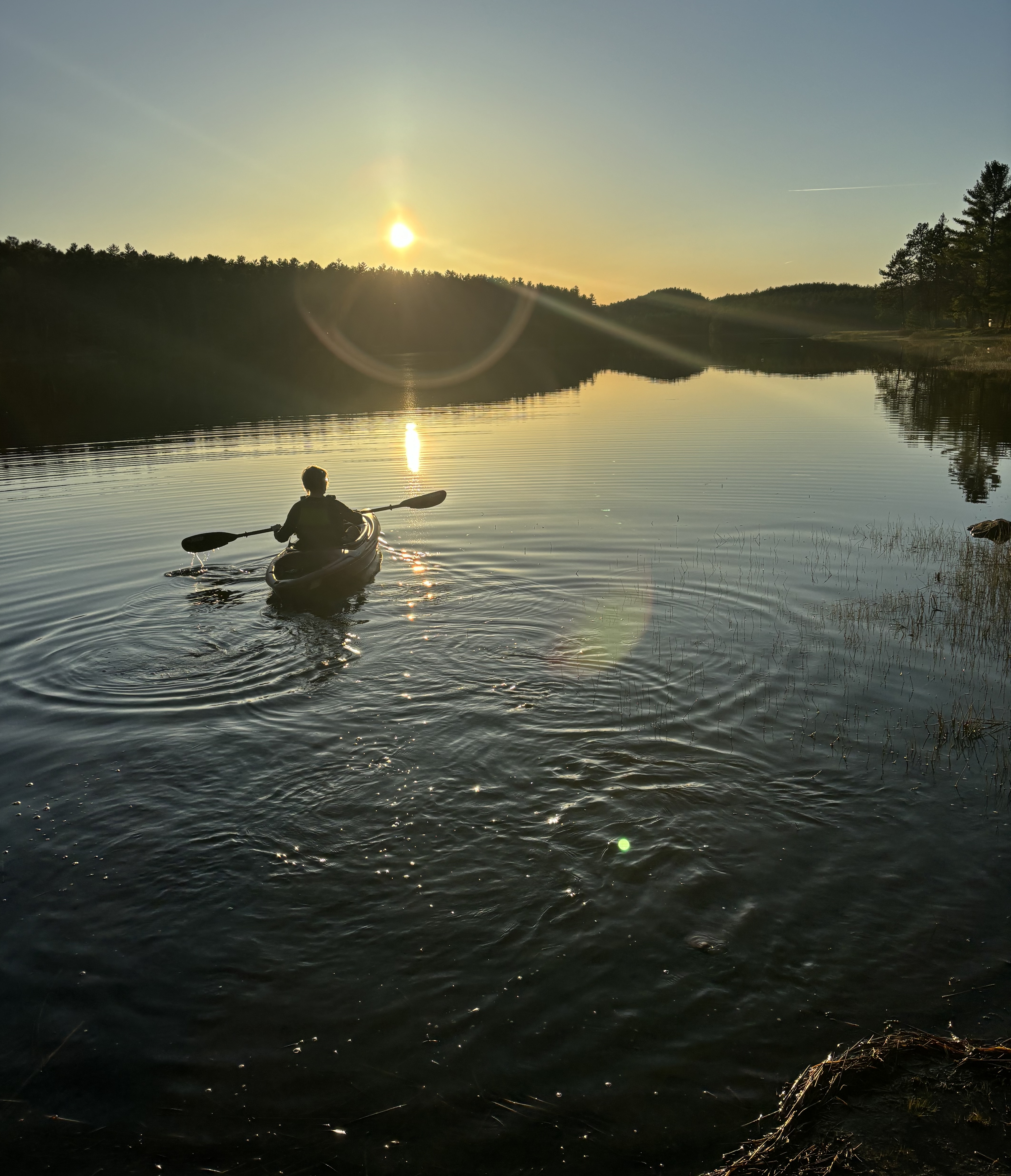 A kayaker paddling on a shining lake at sunset.