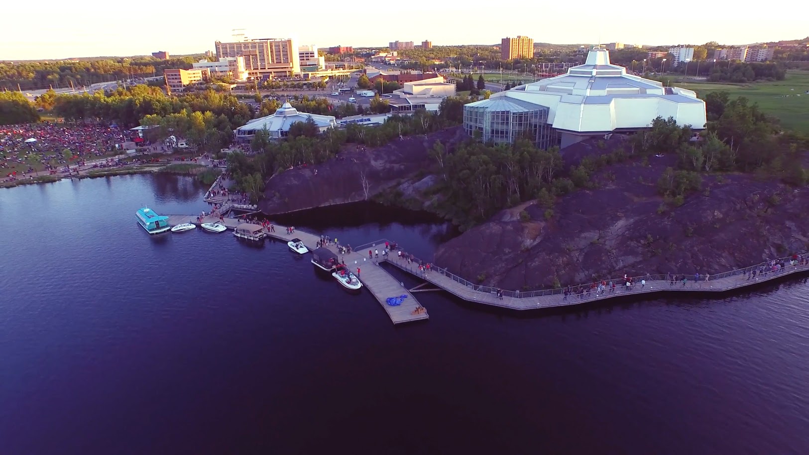 an aerial shot of the huge Science North complex in Sudbury, standing next to a glassy lake and surrounded by trees. 