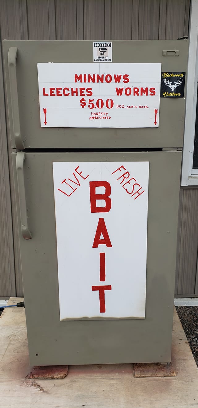 An old fridge placed outdoors with a live bait sign attached to the door.