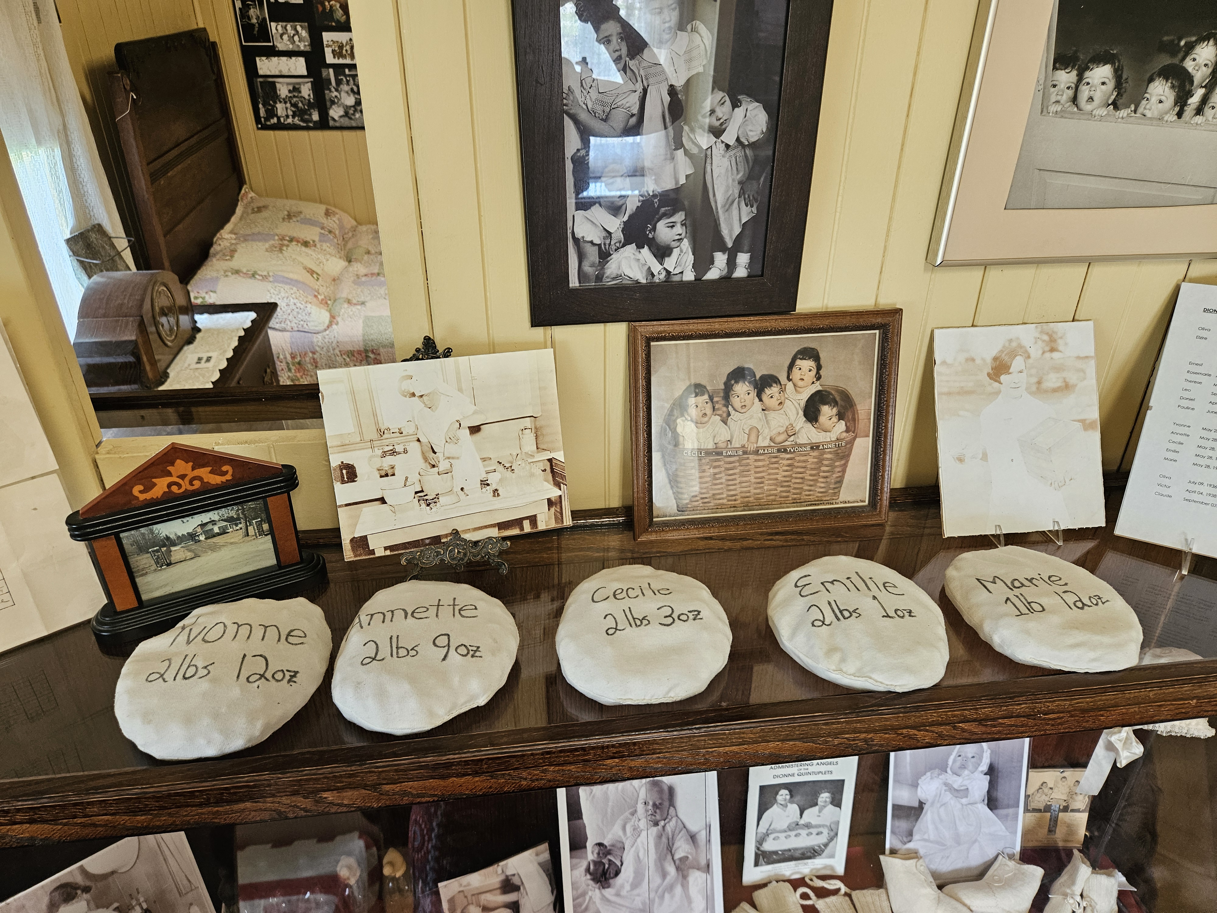 A bedroom display at the Dionne Quintuplets Museum, showing photos of the Quints and 5 clay stones with each girl's name and birth weight carved into them. 