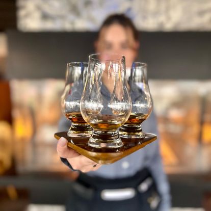 A server holding up a tray of 3 glasses of whiskey