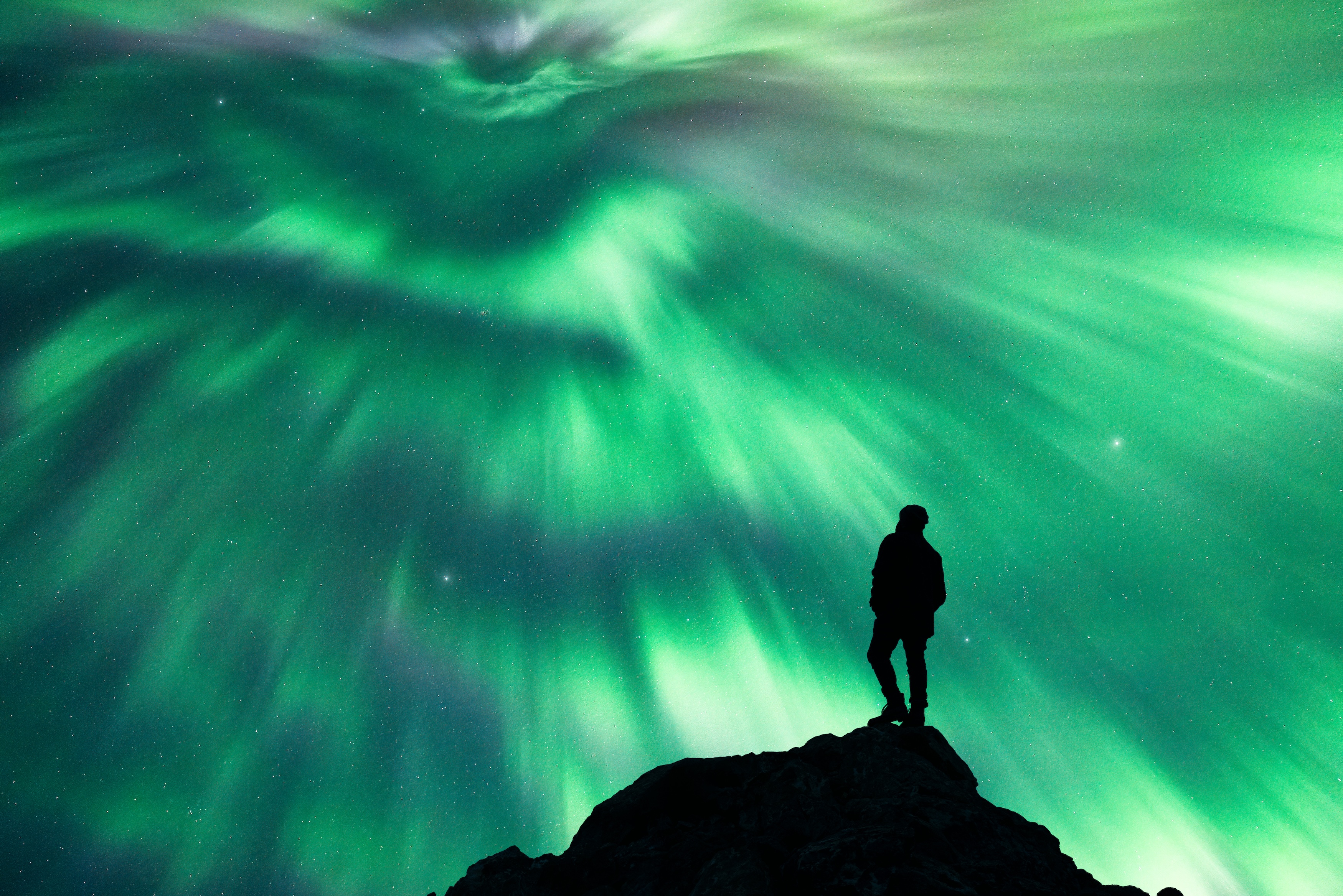 A man stands under a green northern lights diplay. 