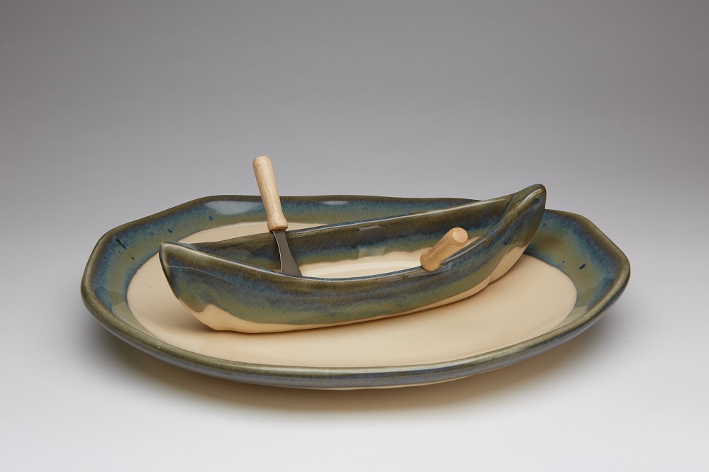 a pottery dip bowl shaped like a canoe on a platter