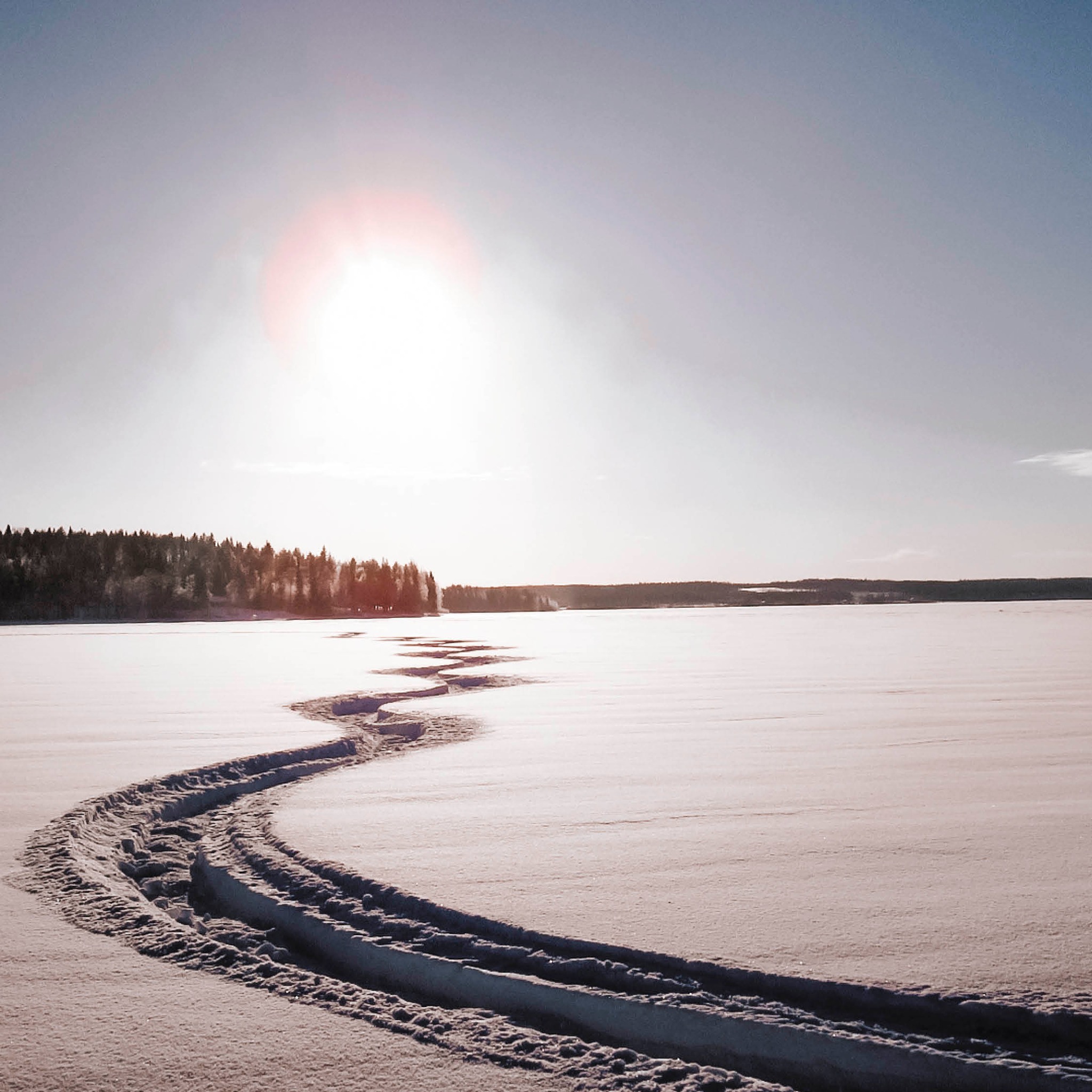 snowmobile tracks on rainy lake with a muted sun in the sky.