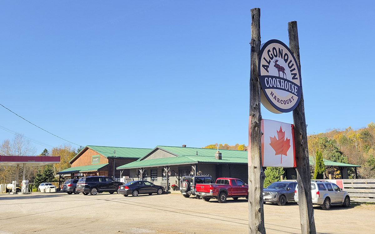 The Algonquin Cookhouse; a single storey diner with green tin roof next to a forested highway in the autumn.