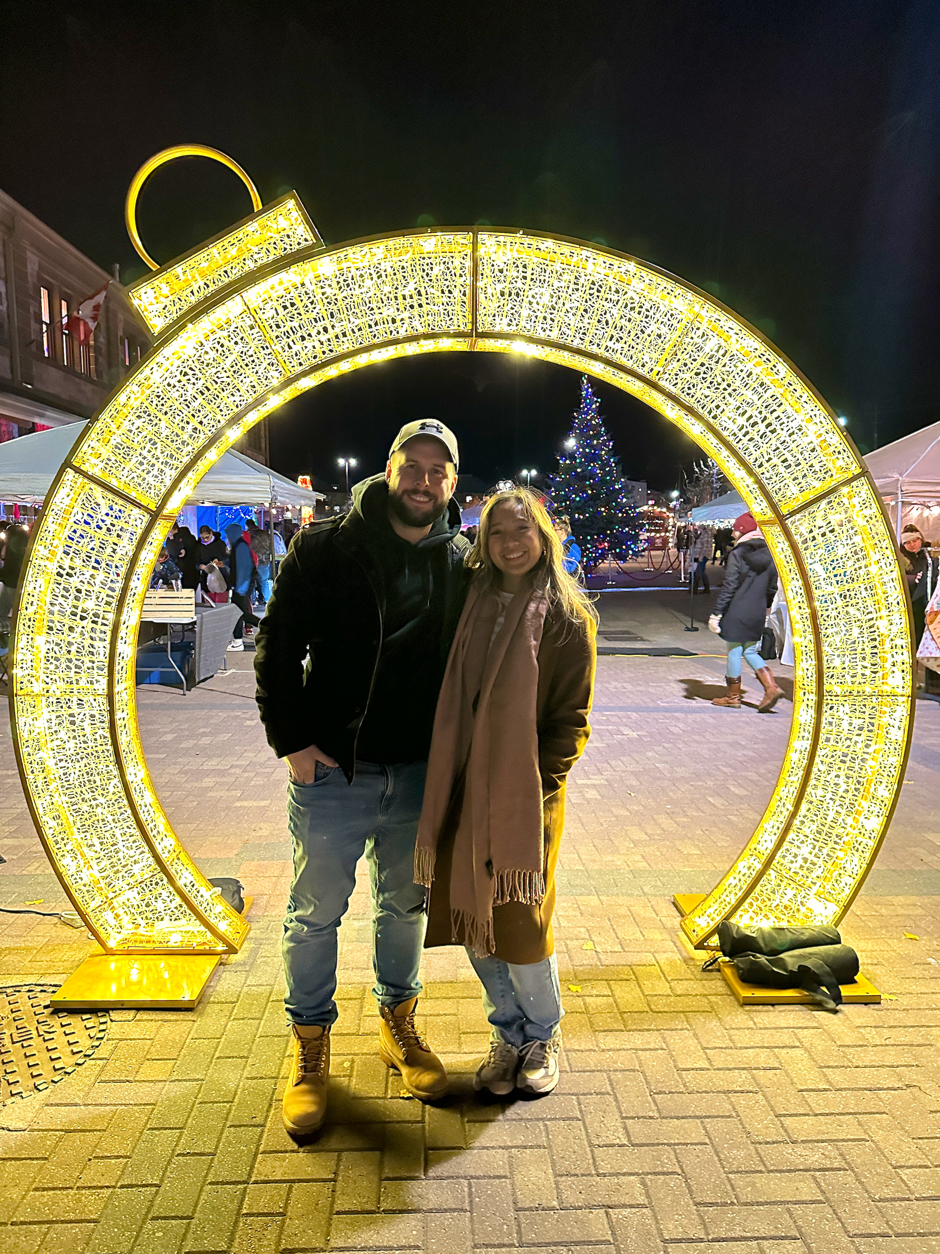 A man and woman in winter clothing standing in front of a decorative light up ornament.