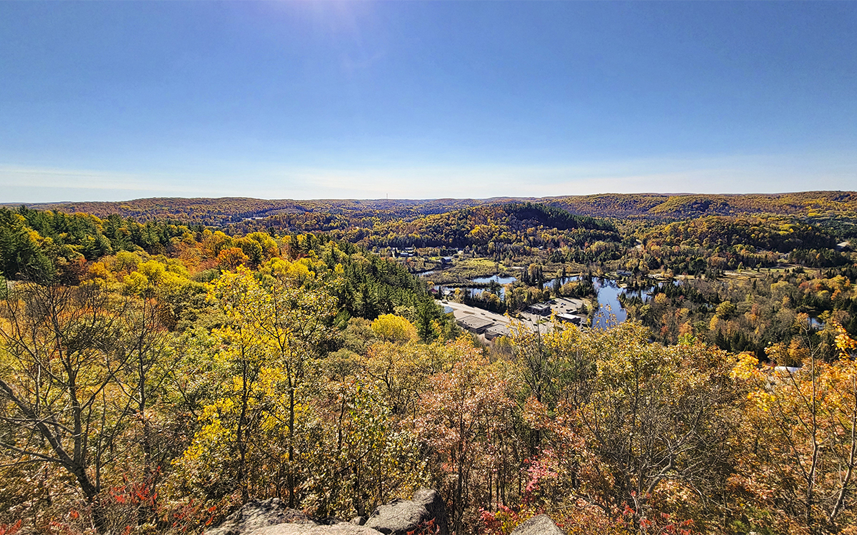 Eagles Nest; a wide valley below filled with a broad expanse of yellow and orange autumn forest, dotted with blue lakes under a clear blue sky.